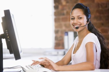 Businesswoman in office wearing headset and typing on computer s clipart