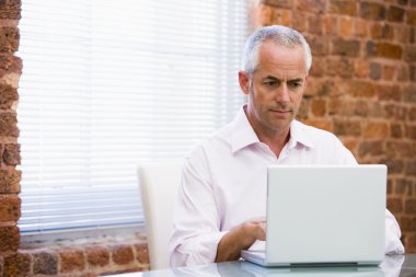 Businessman in office looking at laptop clipart