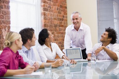 Five businesspeople in boardroom with laptop laughing clipart