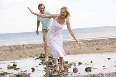 Couple at the beach walking on stones and smiling clipart