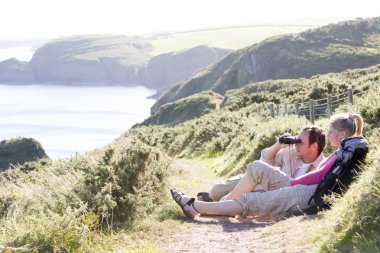 Couple on cliffside outdoors using binoculars and smiling clipart