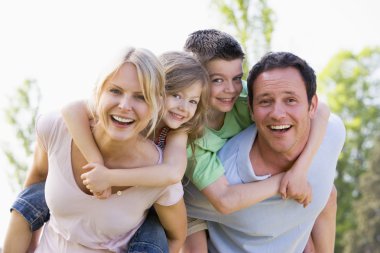 Couple giving two young children piggyback rides smiling clipart