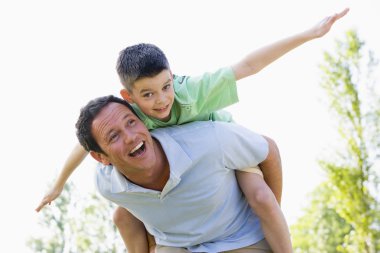 Man giving young boy piggyback ride outdoors smiling clipart