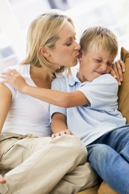 Woman kissing disgusted young boy in living room clipart