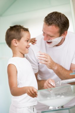 Man in bathroom putting shaving cream on young boy's nose clipart