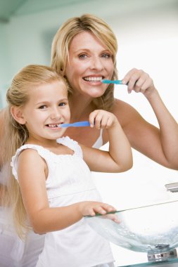 Woman and young girl in bathroom brushing teeth clipart