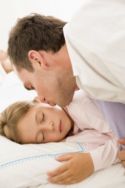 Man waking young girl in bed with kiss clipart