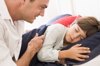 Man waking young boy in bed smiling clipart