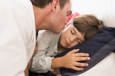 Man waking young boy in bed with kiss clipart