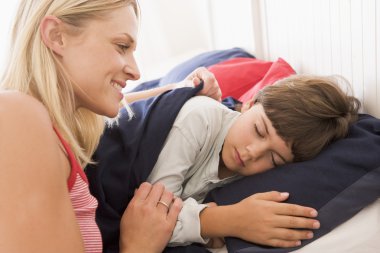 Woman waking young boy in bed smiling clipart