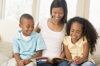 Woman and two children sitting in living room reading book and s clipart