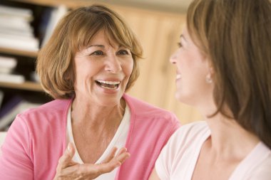 Two women sitting in living room talking and smiling clipart