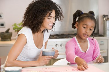 Woman and young girl in kitchen with art project smiling clipart