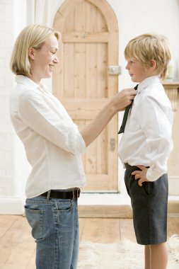 Woman in front hallway fixing young boy's tie and smiling clipart