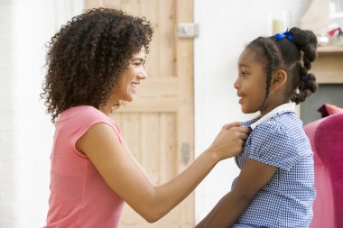 Woman in front hallway fixing young girl's dress and smiling clipart