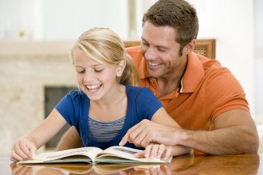 Man and young girl reading book in dining room smiling clipart