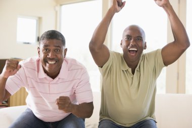 Two men in living room cheering and smiling clipart