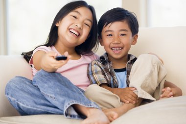 Two youngchildren in living room with remote control smiling clipart