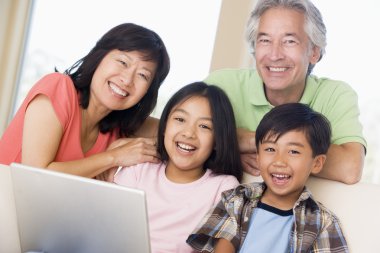 Couple with two young children in living room with laptop smilin clipart