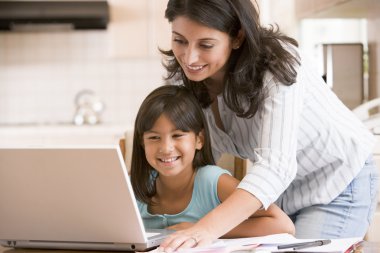 Woman and young girl in kitchen with laptop and paperwork smilin clipart