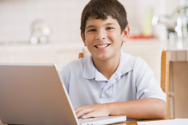 Young boy in kitchen with laptop and paperwork smiling clipart