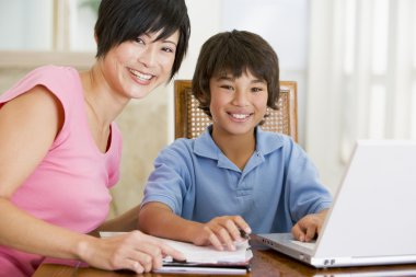 Woman helping young boy with laptop do homework in dining room s clipart