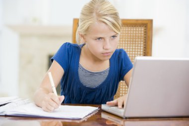 Young girl with laptop doing homework in dining room clipart