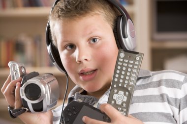 Young boy wearing headphones in bedroom holding many electronic clipart