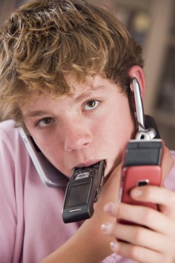 Young boy in bedroom holding many cellular phones clipart