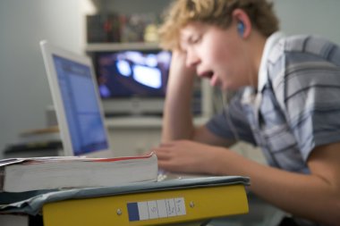 Young boy in bedroom yawning using laptop and listening to MP3 p clipart