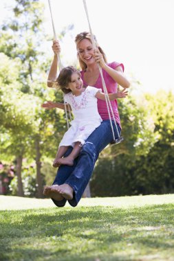 Woman and young girl outdoors on tree swing smiling clipart