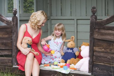 Woman and young girl in shed playing tea and smiling clipart