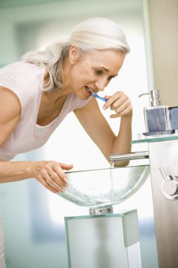 Woman in bathroom brushing teeth clipart