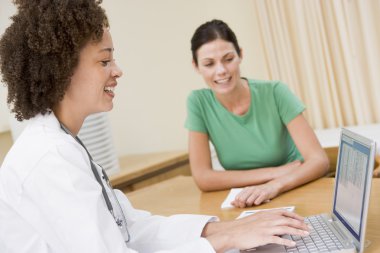 Doctor using laptop with woman in doctor's office smiling clipart