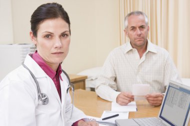 Doctor with laptop and man in doctor's office frowning clipart