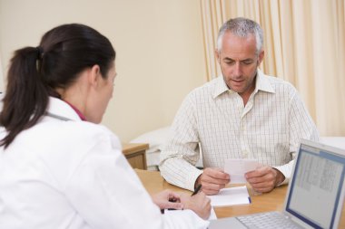 Doctor with laptop and man in doctor's office clipart