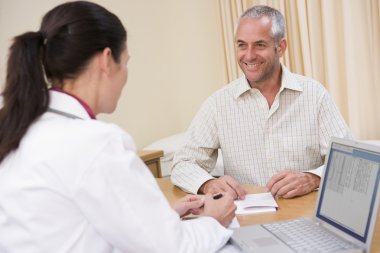 Doctor with laptop and man in doctor's office smiling clipart