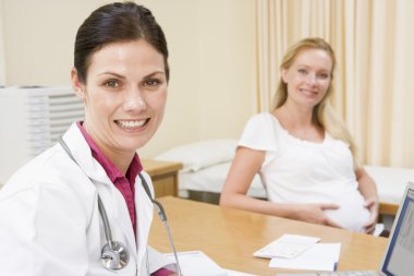 Doctor with laptop and pregnant woman in doctor's office smiling clipart