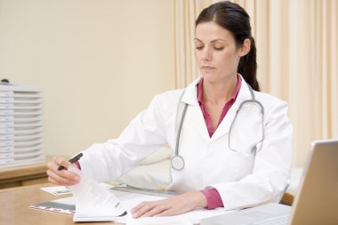 Doctor with laptop writing in doctor's office smiling clipart