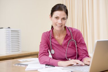 Doctor using laptop in doctor's office smiling clipart