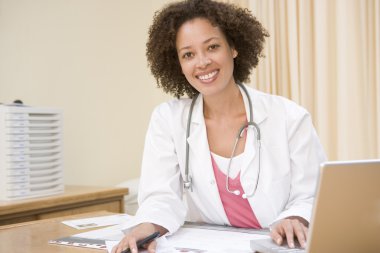 Doctor with laptop in doctor's office smiling clipart