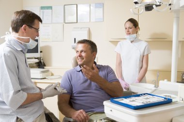 Dentist and assistant in exam room with man in chair smiling clipart