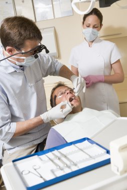 Dentist and assistant in exam room with man in chair clipart