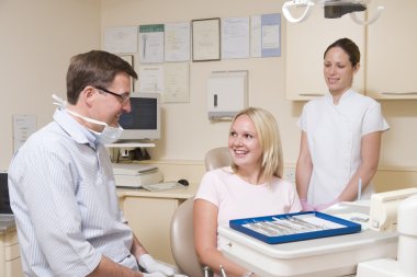 Dentist and assistant in exam room with woman in chair smiling clipart