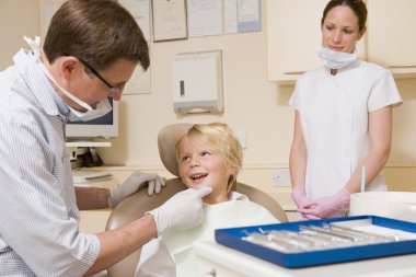 Dentist and assistant in exam room with young boy in chair clipart