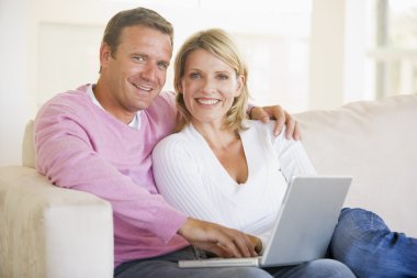 Couple in living room using laptop and smiling clipart