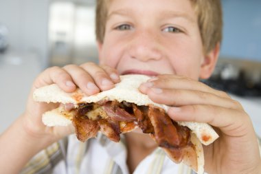 Boy eating bacon sndwich at home clipart