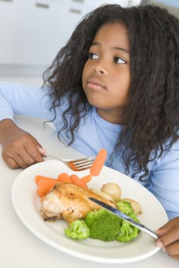 Young girl in kitchen eating chicken and vegetables clipart