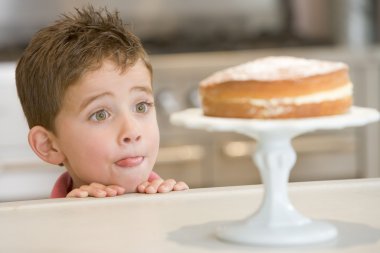 Boy staring longingly at cake at home licking lips clipart