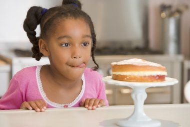 Young girl in kitchen looking at cake on counter clipart